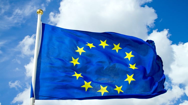 EU:s flagga som syns mot en molnig men solig himmel