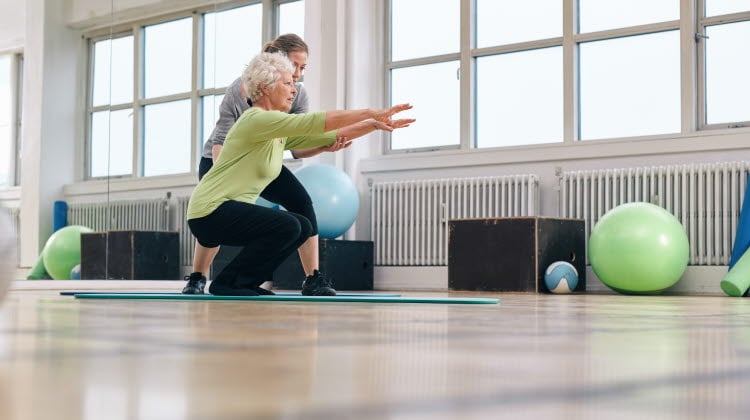 Senior kvinna gör motion med sin personliga tränare på gym. Gym instruktör hjälpa äldre kvinna i hennes träning.