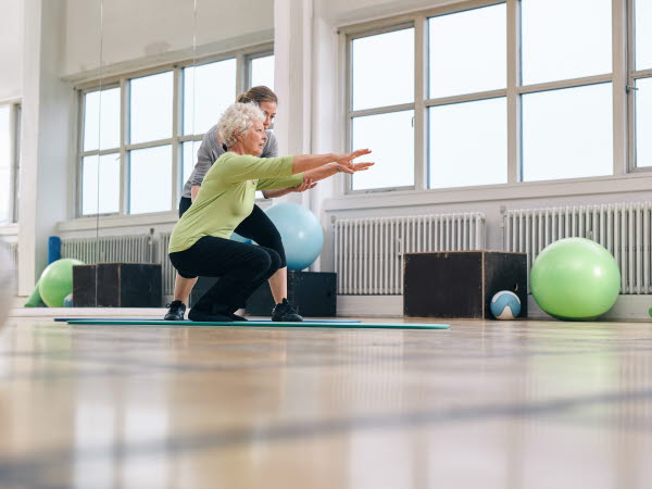 Senior kvinna gör motion med sin personliga tränare på gym. Gym instruktör hjälpa äldre kvinna i hennes träning.